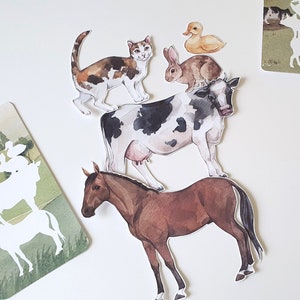 Puede incluir: Un conjunto de recortes de animales, que incluyen un caballo marrón, una vaca blanco y negro, un conejo marrón, un pato amarillo y un gato calico. Los recortes están sobre un fondo blanco.