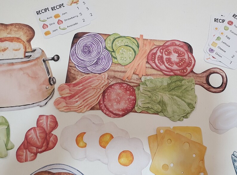 May include: A set of colorful, illustrated food cards for a game. The cards feature images of ingredients like avocado, jam, strawberry, bacon, onion, tomato, cucumber, lettuce, cheese, and eggs. The cards are labeled with the ingredient name and a number.