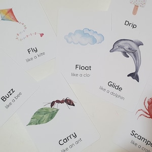 May include: A collection of white flashcards with watercolor illustrations and text. The cards feature images of a kite, bee, cloud, dolphin, ant, worm, crab, and ice cream. Each card has a word and a phrase like "Fly like a kite."