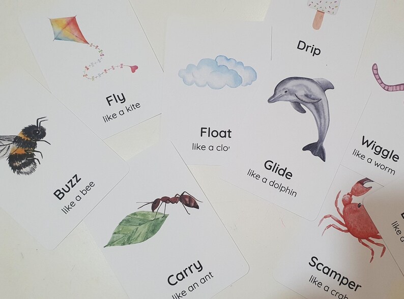 May include: A collection of white flashcards with watercolor illustrations and text. The cards feature images of a kite, bee, cloud, dolphin, ant, worm, crab, and ice cream. Each card has a word and a phrase like "Fly like a kite."