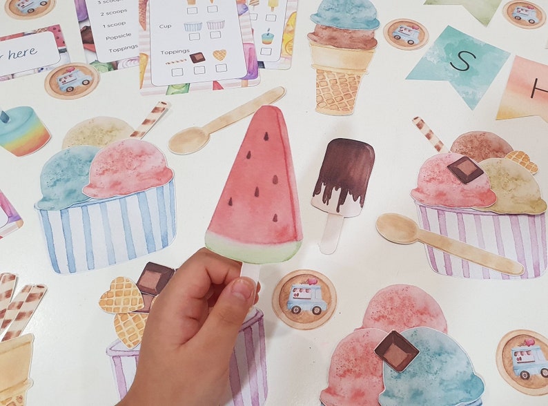 May include: A set of colorful felt ice cream cones, scoops, and toppings for a pretend play ice cream shop. The set includes a watermelon slice, a chocolate popsicle, and a spoon.