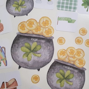 Peut inclure: Deux pots noirs avec des pièces d'or et des trèfles. Le plus grand pot porte l'inscription "large" et le plus petit pot porte l'inscription "medium". Il y a aussi plusieurs pièces d'or éparpillées autour des pots.