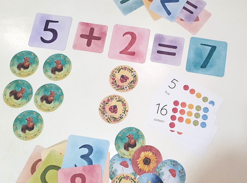 May include: A set of colorful cards with numbers and symbols, including a plus sign, an equals sign, and the numbers 5, 2, and 7. The cards are arranged in a row, with the equation 5 + 2 = 7 written out. There are also several small, round, colorful stickers with images of animals and insects.