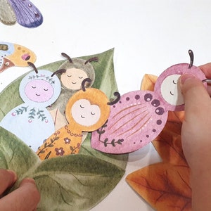 May include: A set of four felt butterfly figures with different colors and patterns. The butterflies are arranged on a green leaf with a brown leaf in the background.