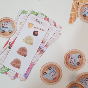 May include: A set of ice cream recipe cards with illustrations of ice cream scoops, cones, and a chocolate bar. The cards have a pink and white striped pattern and the word "Recipe" is printed on the top card.