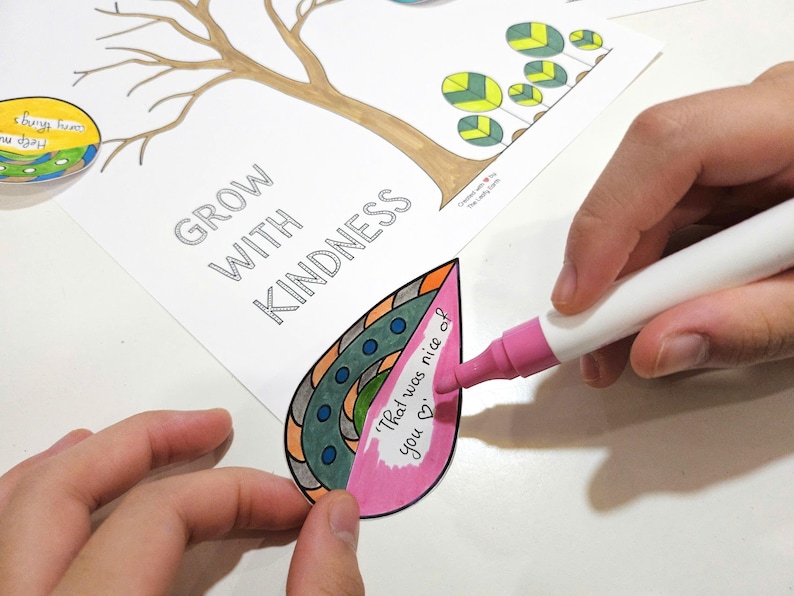 May include: A person coloring a leaf-shaped paper cutout with a pink marker. The cutout has a decorative design and the text "That was nice of you". The words "Grow with Kindness" are printed on the paper.