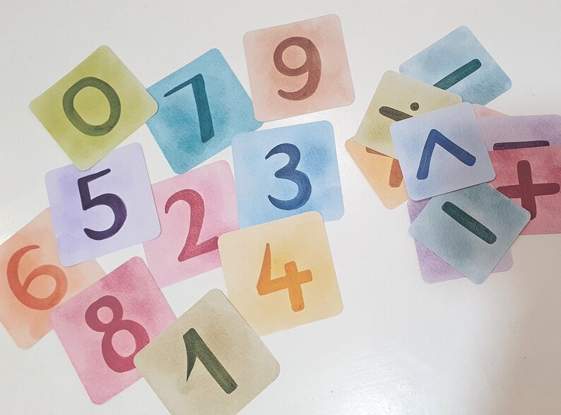 May include: A set of colorful, square cards with numbers 1 through 9 and math symbols, including plus, minus, and division signs. The cards are made of thick paper and have a watercolor-like finish.