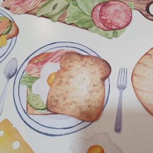 May include: A watercolor illustration of a breakfast sandwich with bacon, egg, and avocado on a plate. The sandwich is on a white background with a fork and spoon.