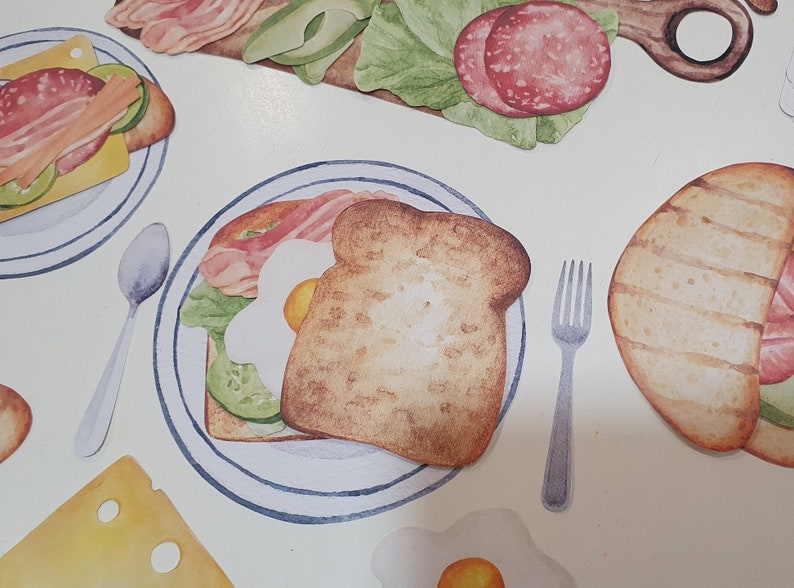 May include: A watercolor illustration of a breakfast sandwich with bacon, egg, and avocado on a plate. The sandwich is on a white background with a fork and spoon.