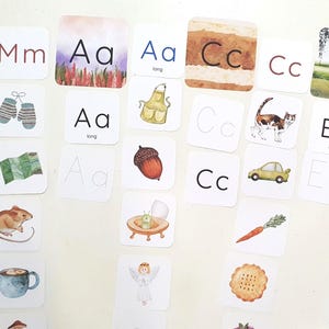 May include: A collection of square flashcards featuring watercolor illustrations and letters of the alphabet. Each card displays a letter, a corresponding image, and the word's beginning letter. The cards are designed for early learning.