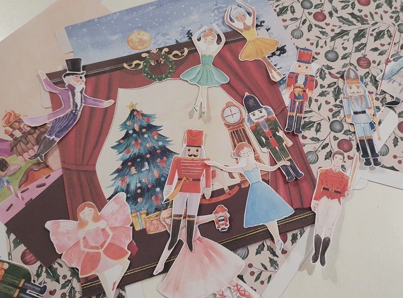 May include: A set of colorful Christmas-themed paper cutouts featuring a Christmas tree, nutcracker soldiers, ballerinas, and a clock. The cutouts are on a white background.