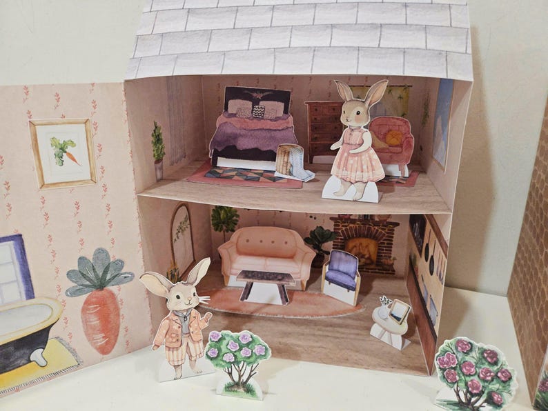 May include: A two-story dollhouse with a pink couch, a bed with a purple comforter, and a fireplace. There are two bunny figurines, one in a pink dress and one in a brown vest. The dollhouse is decorated with floral accents.