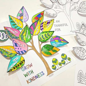 May include: A colorful paper tree with leaves, each decorated with unique patterns and inspirational messages. The tree trunk is brown, and the leaves are various colors. The words "GROW WITH KINDNESS" are at the base of the tree.