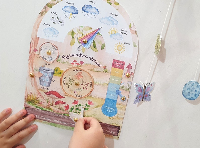 May include: A colorful weather station for kids with a rainbow umbrella, clouds, a thermometer, and a wheel showing the seasons. The station is made of cardboard and has a whimsical design.