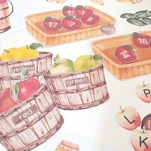 May include: A set of printable educational materials for kids featuring images of apples in baskets and buckets. The images include red, green, and yellow apples, as well as numbers and letters. The text on the images includes "odd", "greater than", "yellow", "red", "green", "13", "7", "17", "14", "18", "6", "L", "K", "P", "P", "r", "f", "9".