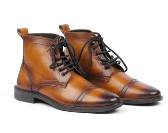 May include: A pair of brown leather lace-up boots with black laces. The boots have a cap toe design and a slightly distressed finish.