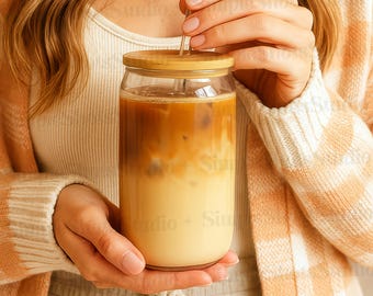 Op de afbeelding: Een persoon die een helder glas met een houten deksel vasthoudt gevuld met ijskoffie. Een glazen rietje zit in de koffie.