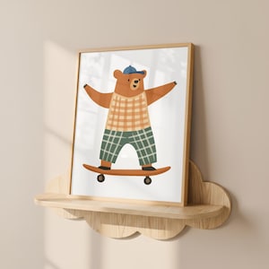 K&ouml;nnte beinhalten: Gerahmter Druck mit einem braunen B&auml;ren auf einem Skateboard. Der B&auml;r tr&auml;gt eine blaue Kappe, ein kariertes Hemd und eine gr&uuml;ne karierte Hose. Das Skateboard ist braun. Das Kunstwerk befindet sich auf einem Holzregal.