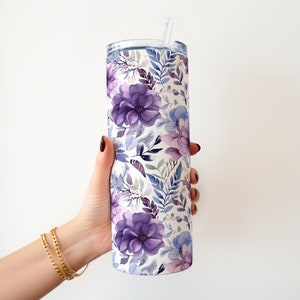 May include: A stainless steel tumbler with a floral pattern in shades of purple and blue. The tumbler has a lid and a straw.