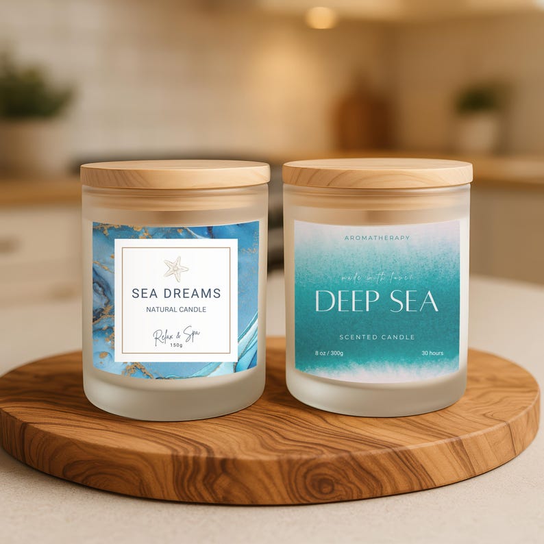 Może przedstawiać: Dwie świece do aromaterapii ze szkła mrożonego z drewnianymi pokrywkami na drewnianej tacy. Jedna świeca głosi "Sea Dreams" z niebiesko-złotym wzorem. Druga głosi "Deep Sea" z turkusowym wzorem. Każda świeca ma 300g.