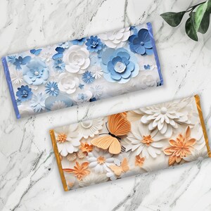 Pu&ograve; includere: Due involucri di barrette di cioccolato con un design floreale. L'involucro superiore presenta fiori di carta blu e bianchi. L'involucro inferiore presenta fiori di carta bianchi e arancioni con farfalle.