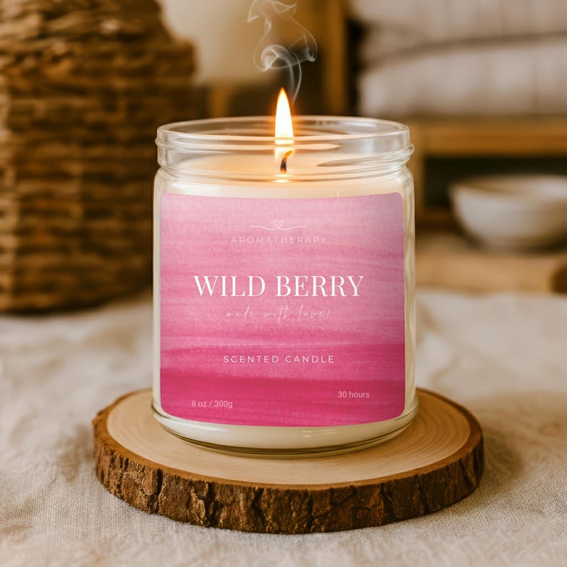 Op de afbeelding: Een brandende geurkaars in een glazen pot met een roze label met de tekst "Wild Berry". De kaars staat op een houten onderzetter. Het label zegt ook "Aromatherapie" en "Geurkaars". De kaars is 300g en brandt 30 uur.