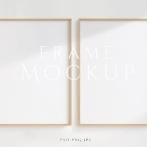 Puede incluir: Dos marcos de fotos vacíos de madera clara sobre un fondo blanco. Los marcos están uno al lado del otro y el texto "FRAME MOCKUP" está escrito en blanco en el centro de la imagen.