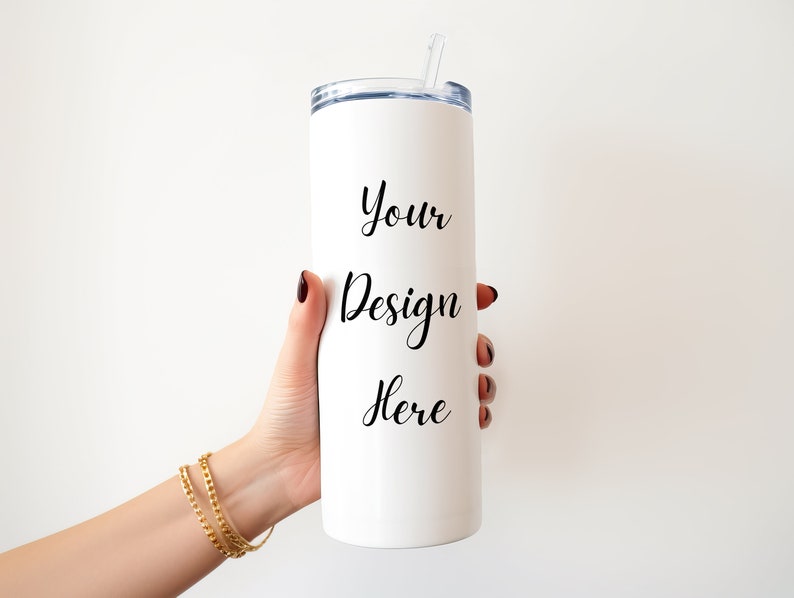 May include: White stainless steel tumbler with a black inscription that reads "Your Design Here". The tumbler has a clear lid and a straw.