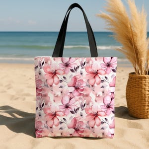Puede incluir: Una bolsa de tela rosa y blanca con un estampado floral. La bolsa tiene asas negras y est&aacute; hecha de lona.