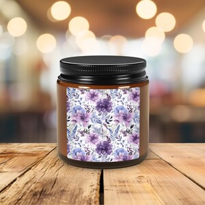May include: A brown glass candle jar with a black lid. The jar has a label with a purple and blue floral pattern.