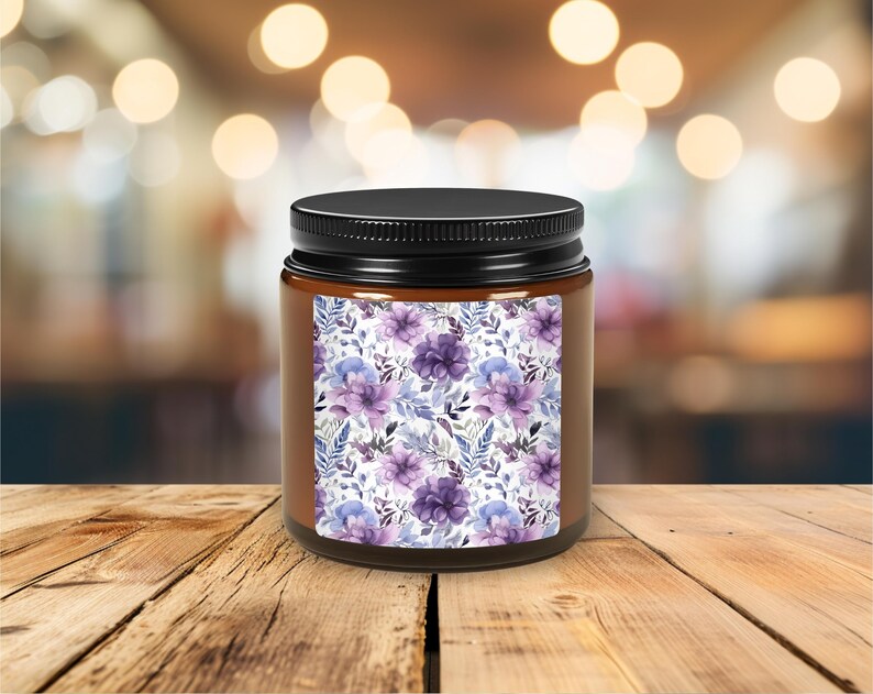 May include: A brown glass candle jar with a black lid. The jar has a label with a purple and blue floral pattern.