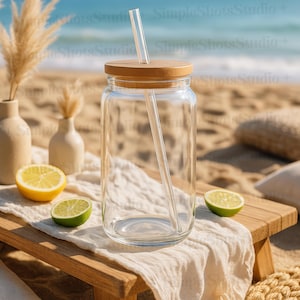Könnte beinhalten: Ein klares Glasgefäß mit einem Holzdeckel und einem Glasstrohhalm. Das Gefäß steht auf einem weißen Tuch auf einem Holztisch. Auf dem Tisch liegen Zitronen und Limetten.