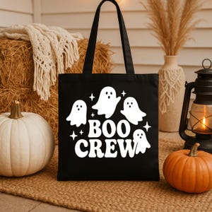 Op de afbeelding: Zwarte draagtas met een witte afbeelding van vier cartoongeesten en de woorden "BOO CREW". De tas heeft twee zwarte handvatten. De afbeelding bevat pompoenen en een lantaarn, perfect voor Halloween.