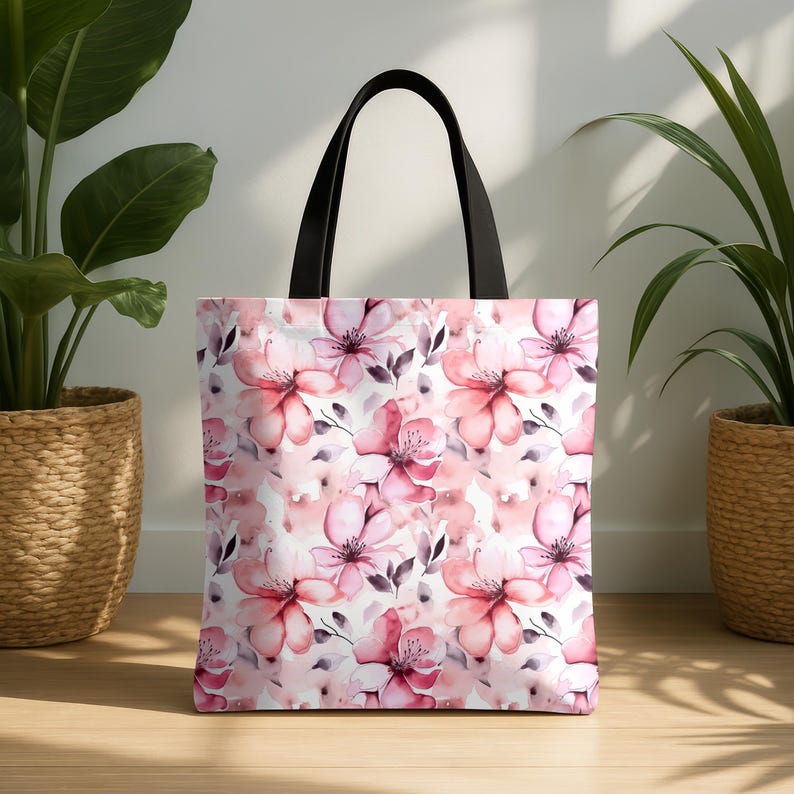 May include: A white tote bag with black handles features a pink floral pattern. The flowers are watercolor-style and have a soft, romantic feel.