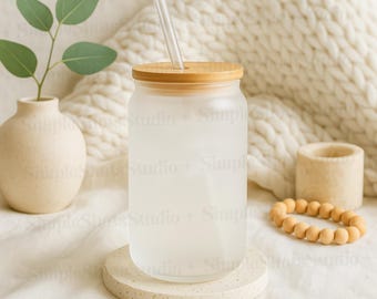 May include: A frosted glass tumbler with a bamboo lid and a clear drinking straw. The tumbler is sitting on a beige coaster and is surrounded by a white knitted blanket.