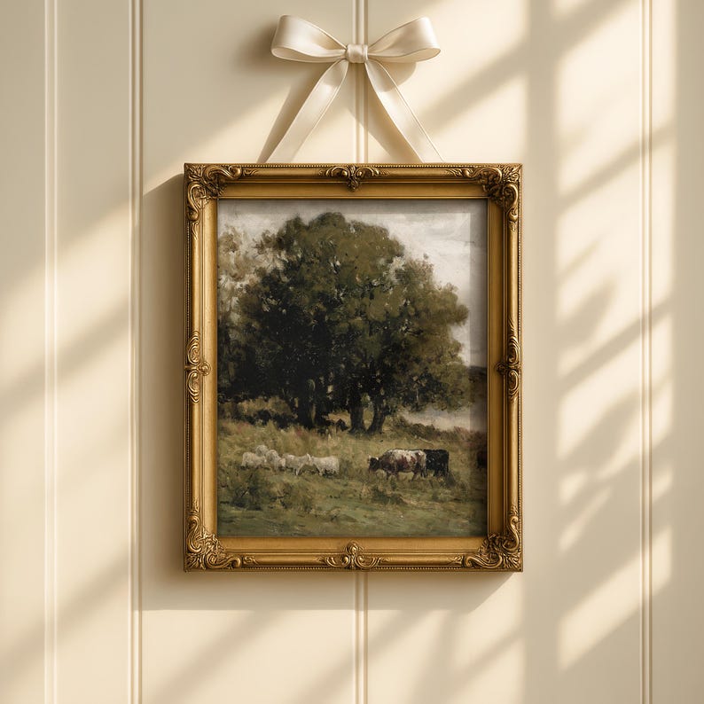 Op de afbeelding: Een ingelijst landschapsschilderij met een gouden, sierlijke lijst, dat een boom, schapen en koeien in een veld afbeeldt. Het schilderij is opgehangen met een cr&egrave;mekleurig lint dat in een strik is geknoopt.