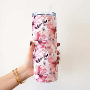 May include: A stainless steel tumbler with a pink and white floral design. The tumbler has a lid and a straw.