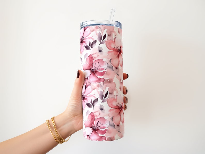 May include: A stainless steel tumbler with a pink and white floral design. The tumbler has a lid and a straw.