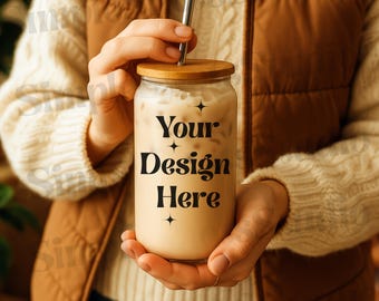 Op de afbeelding: Een persoon houdt een helder glas vast met een bamboe deksel en een rietje. Het glas is gevuld met een lichtbruine vloeistof en heeft de tekst "Your Design Here" erop gedrukt.