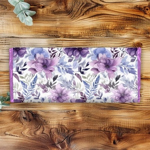 Pu&ograve; includere: Un tessuto con stampa floreale viola e blu su sfondo bianco. Il tessuto ha un bordo viola chiaro.
