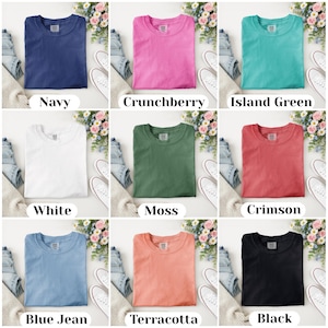 Puede incluir: Presentaci&oacute;n de nueve camisetas de diferentes colores, cada una doblada cuidadosamente. Los colores incluyen azul marino, rosa, turquesa, blanco, verde, rojo, azul claro, melocot&oacute;n y negro. Cada camisa est&aacute; etiquetada con el nombre de su color.