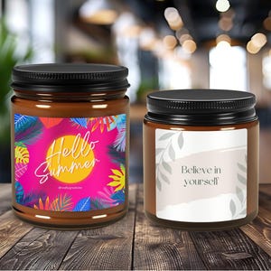 May include: Two brown glass candle jars with black lids. The jar on the left has a pink, yellow, and green label with the text "Hello Summer". The jar on the right has a white label with the text "Believe in yourself".