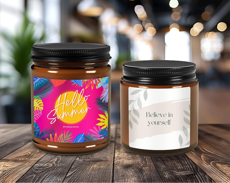 May include: Two brown glass candle jars with black lids. The jar on the left has a pink, yellow, and green label with the text "Hello Summer". The jar on the right has a white label with the text "Believe in yourself".