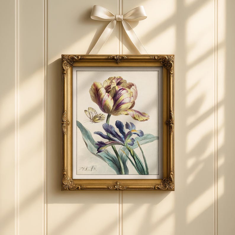 Op de afbeelding: Een ingelijste botanische prent met een gedetailleerde illustratie van een tulp, iris en vlinder. Het kunstwerk zit in een gouden, sierlijke lijst, opgehangen aan een cr&egrave;mekleurig lint. De bloemen zijn in tinten paars, geel en blauw.