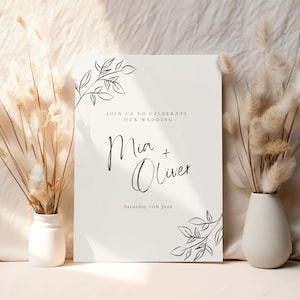 May include: A white wedding invitation with black calligraphy that reads "Join us to celebrate our wedding Mia + Oliver Saturday 5th June". The invitation is decorated with simple black line drawings of leaves and branches.