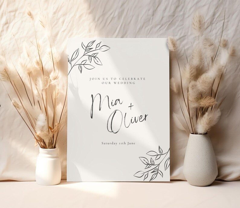 May include: A white wedding invitation with black calligraphy that reads "Join us to celebrate our wedding Mia + Oliver Saturday 5th June". The invitation is decorated with simple black line drawings of leaves and branches.