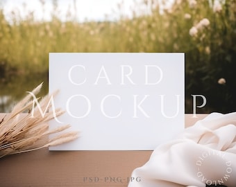 May include: A white card mockup with the text "CARD MOCKUP" on a brown surface with dried grass and a white fabric.