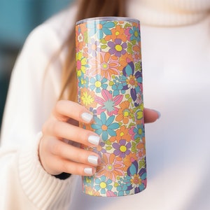 May include: A stainless steel tumbler with a colorful floral pattern. The pattern features a variety of flowers in shades of pink, blue, yellow, and orange on a cream background.