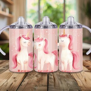 Peut inclure: Trois gobelets &agrave; bec avec un motif de licorne sur fond rose. Les licornes ont des crini&egrave;res, des queues roses et des cornes dor&eacute;es. Les gobelets ont des couvercles transparents, des poign&eacute;es blanches et sont pos&eacute;s sur une surface en bois.