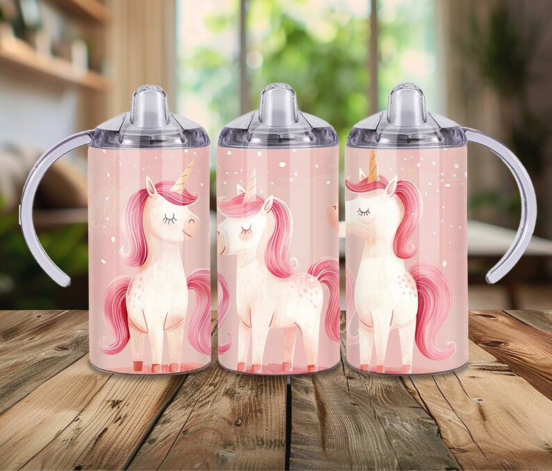 Peut inclure: Trois gobelets &agrave; bec avec un motif de licorne sur fond rose. Les licornes ont des crini&egrave;res, des queues roses et des cornes dor&eacute;es. Les gobelets ont des couvercles transparents, des poign&eacute;es blanches et sont pos&eacute;s sur une surface en bois.
